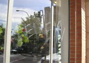 A scratched word "FEVER" is visible on a glass window of a building, with a street scene reflection showing trees, cars, and a brick wall on the right.