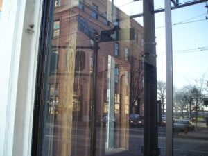 Reflection of buildings and a street sign seen through the glass window of a storefront on a city street.