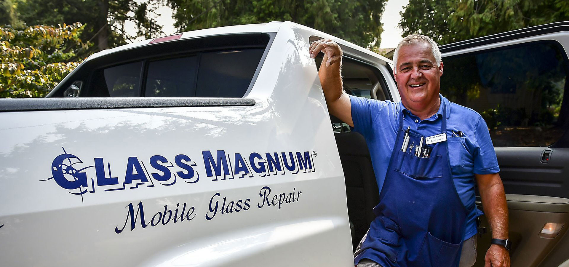 A man in a blue shirt stands smiling next to a white vehicle with the text "Glass Magnum Mobile Glass Repair" on the side.